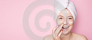 Smiling woman with a towel on her head on a pink background and face cream. Hydration of the skin, skin care face, beauty