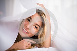 Smiling woman under a duvet in her bedroom