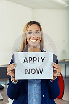 Smiling woman urging people to Apply Now holding up a sign