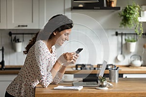 Smiling woman use smartphone at home kitchen