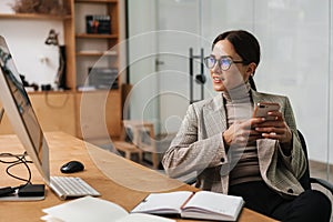 Smiling woman using cellphone while working with computer and planner