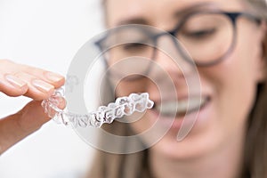 smiling woman using clear plastic removable braces aligner or whitening tray. dental orthodontic care