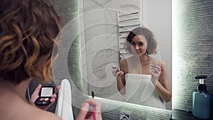 Smiling woman using eyebrow shadows make up in front mirror. Happy female using beauty cosmetics to improve herself
