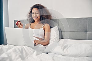 Smiling woman using her computer in bed