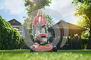 Smiling woman using lawn mower while working at garden