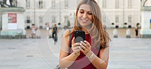 Smiling woman using mobile phone app to play online. City woman relaxing. Urban lifestyle. Banner crop for advertising copy space