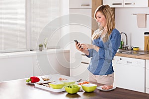 Smiling Woman Using Mobilephone In Kitchen