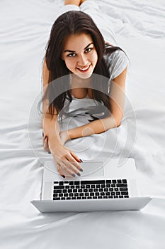 Smiling woman using a notebook on her bed