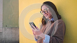 Smiling woman using smartphone against yellow wall outside