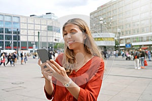 Smiling woman using smartphone in Alexanderplatz square in Berlin, Germany