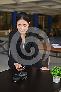 Smiling woman using smartphone for payment to in coffee shop.