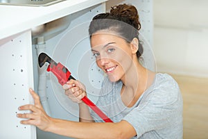 smiling woman using wrench under kitchen sink