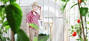 Smiling woman in vegetable garden on white wooden shed background with gardening tools, cherry tomatoes plants in the foreground