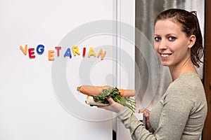 Smiling woman with vegetables in the kitchen, fridge with word v