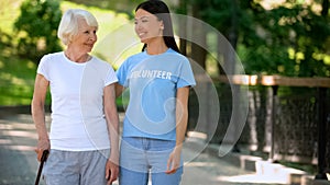 Smiling woman volunteer t-shirt and happy aged lady walking nursing home garden