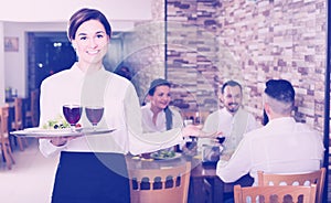 Smiling woman waitress carrying order for visitors