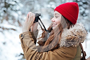 Smiling woman walking and taking pictures in winter forest