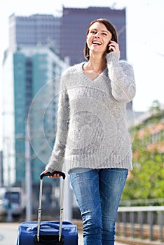 Smiling woman walking and talking on mobile phone with suitcase