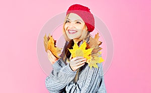 Smiling woman in warm clothes with yellow leaves. Autumn girl in red hat, knitted sweater and scarf.