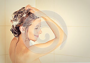 Smiling woman washing head with shampoo in a shower photo