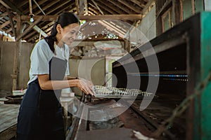 smiling woman wearing an apron tossing the pan of cake batter into the oven