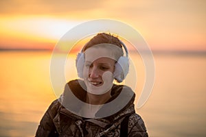 Smiling woman wearing ear muffs at sunset