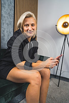 smiling woman wearing an elbow brace sitting on the sofa and holding a phone, vertical shot