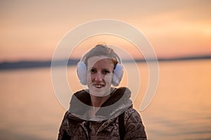 Smiling woman wearing fluffy ear muffs at sunset