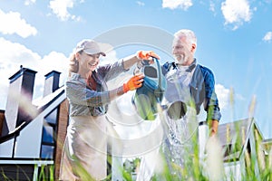 Smiling woman wearing peaked cap joining her husband watering plants