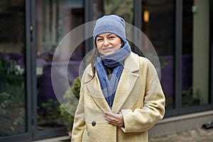 Smiling woman wearing stylish coat in city. Blue knitted hat and scarf. Happy mood