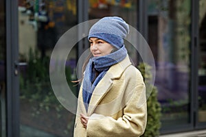 Smiling woman wearing stylish coat in city. Blue knitted hat and scarf. Happy mood