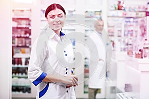 Smiling woman wearing white uniform working as a druggist in a pharmacy