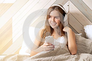 Smiling woman wearing wireless headphones listen to music in bed