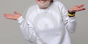 Smiling woman in white longsleeve spreads her hands, showing her clothes. Text space. No face. Isolated on white .