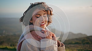 Smiling woman windblown hair posing at cold evening coastal hill closeup.