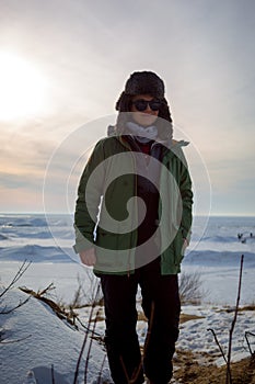 Smiling woman in winter clothes on frozen lake shore during sun