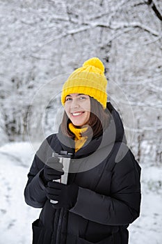 smiling woman in winter outfit drinking warm up drink from refillable mug