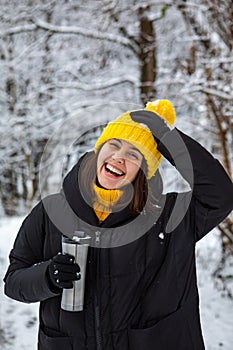 smiling woman in winter outfit drinking warm up drink from refillable mug