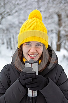 smiling woman in winter outfit drinking warm up drink from refillable mug