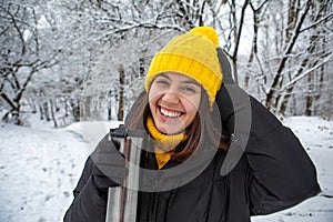 smiling woman in winter outfit drinking warm up drink from refillable mug