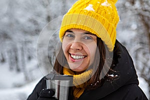 smiling woman in winter outfit drinking warm up drink from refillable mug