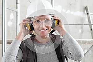 Smiling woman worker portrait wearing helmet, safety glasses and hearing protection headphones, scaffolding interior construction photo