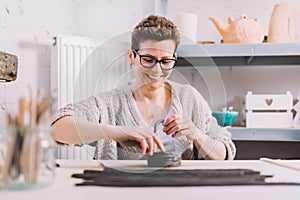 Smiling woman working with clay in pottery ceramics workshop