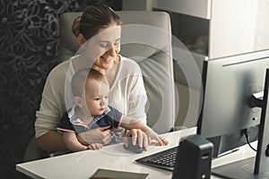 Smiling woman working at computer with her little baby son