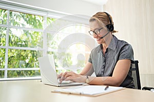 Smiling woman in working on laptop and headset in call center