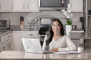 A smiling woman works from her home office in her kitchen