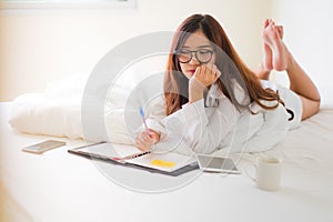 Smiling woman writing notes lying in bed