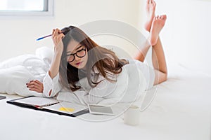 Smiling woman writing notes lying in bed