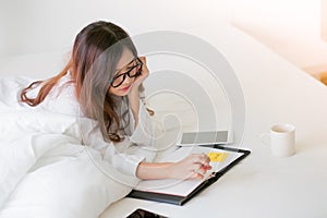 Smiling woman writing notes lying in bed