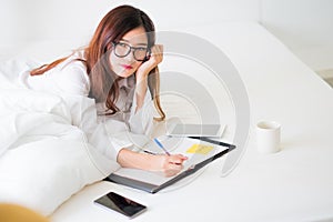 Smiling woman writing notes lying in bed